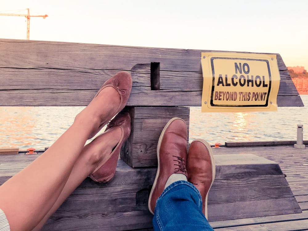 2 people with feet up on bench no alcohol beyond this point sign