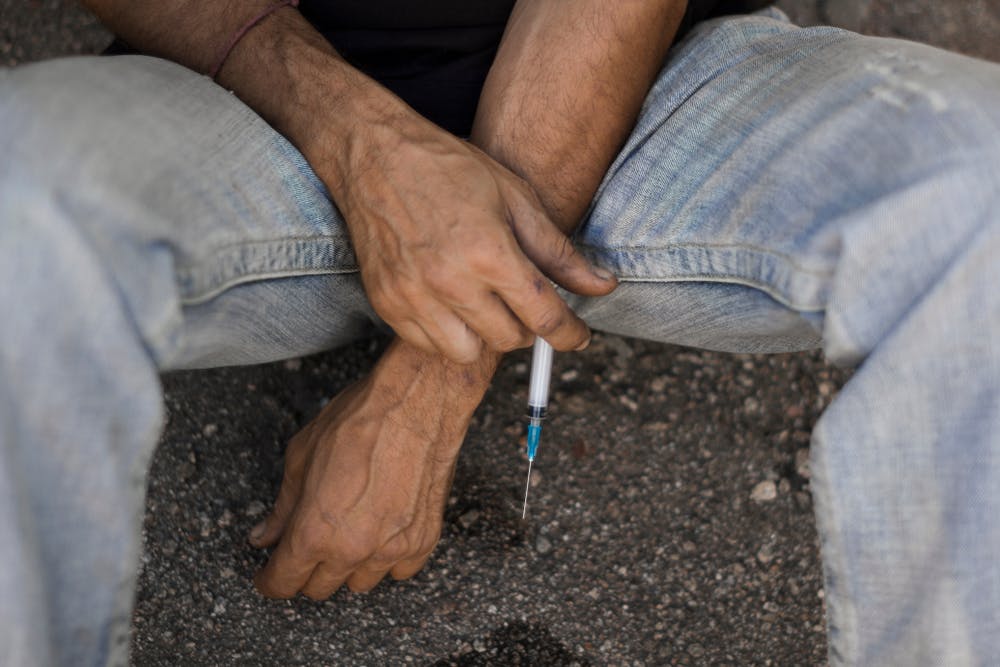 Drug addicted man in jeans sitting on the ground with syringe in his hands